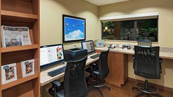 A workspace with two desks, computers, chairs, a window with a view, and a shelf with books.