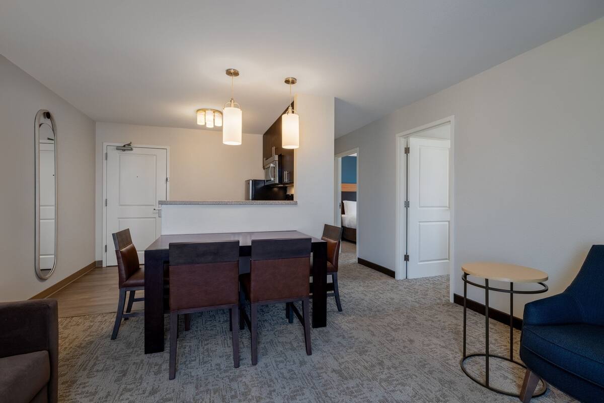 A modern kitchen with dark countertops, a dining area with a rectangular table and chairs, and a small round table with a blue chair.