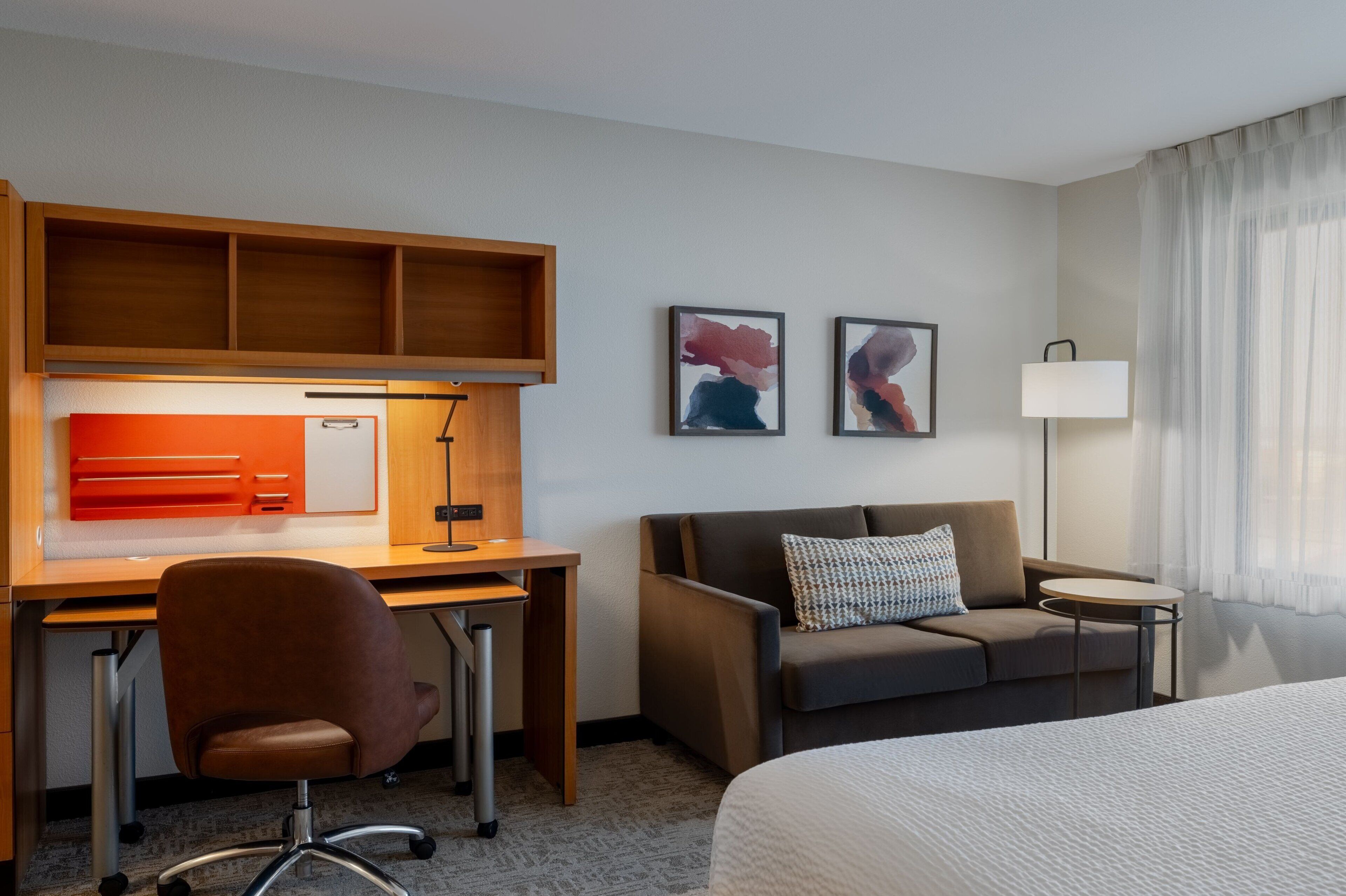 A hotel room with a bed, a desk with a chair, a sofa, a small table, and two framed pictures on the wall.