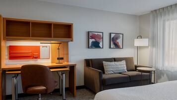 A hotel room with a bed, a desk with a chair, a sofa, a small table, and two framed pictures on the wall.