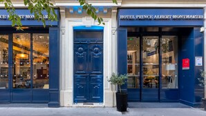 Exterior del Hotel Prince Albert Montmartre, con amplios ventanales y una puerta azul destacada.