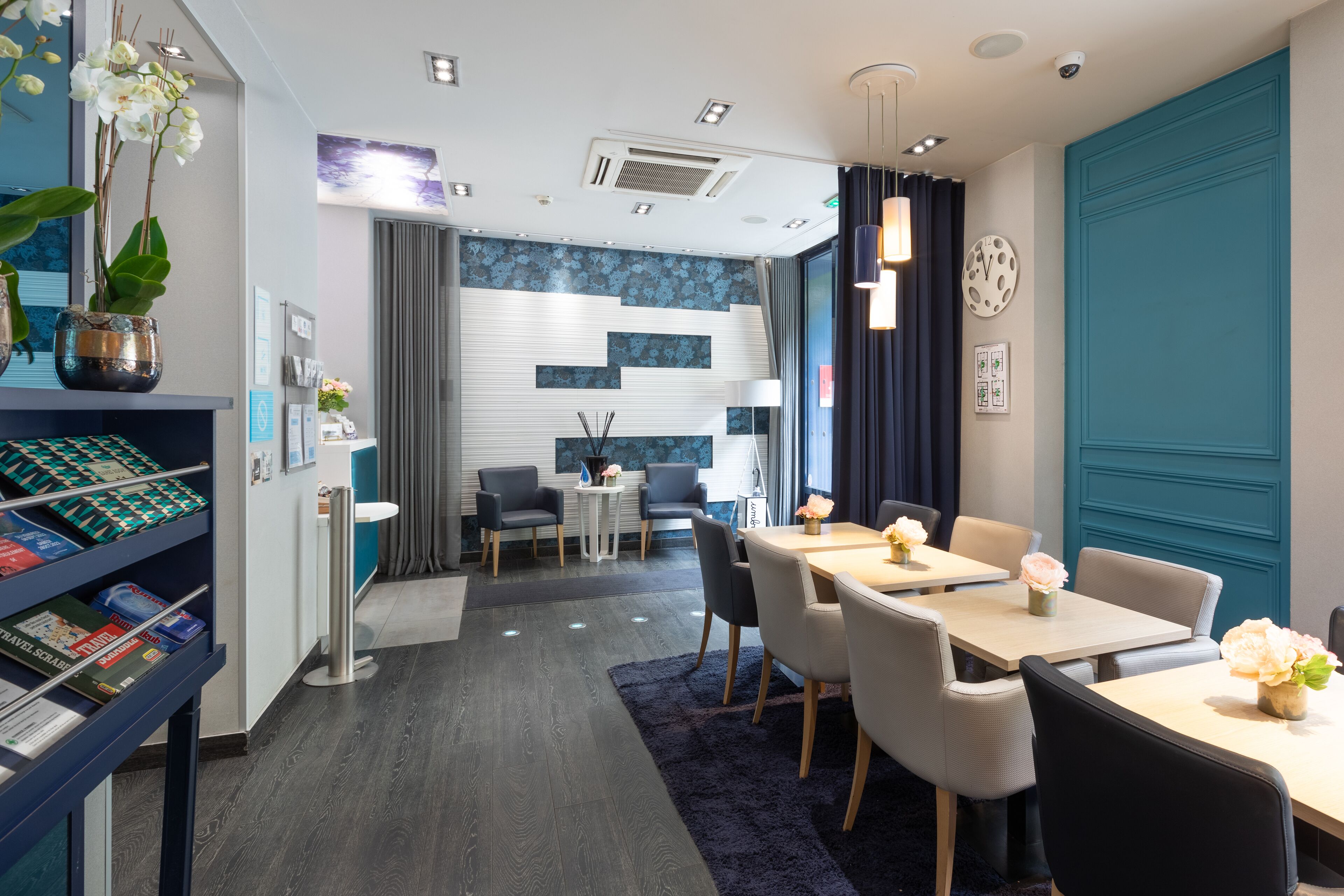 Una habitación de hotel moderna con comedor, una estantería con revistas y una planta decorativa.