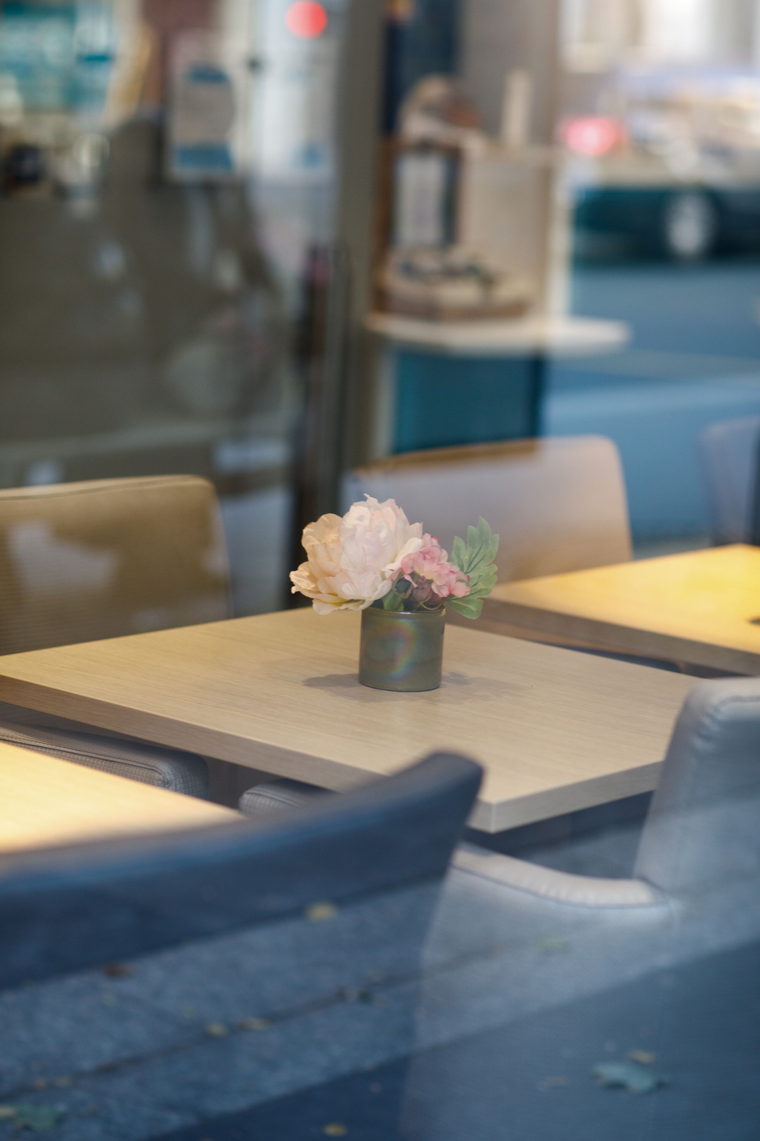 Un comedor con una mesa dispuesta para dos, un florero con flores y un fondo desenfocado que sugiere un ambiente de restaurante.
