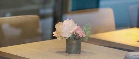 Un comedor con una mesa dispuesta para dos, un florero con flores y un fondo desenfocado que sugiere un ambiente de restaurante.