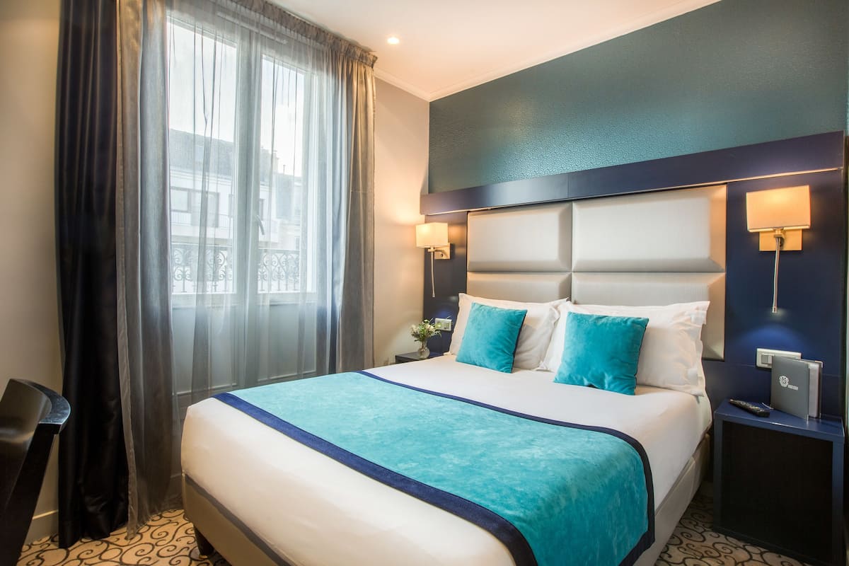 A hotel room with a large bed, a nightstand, a desk, and a window with curtains.