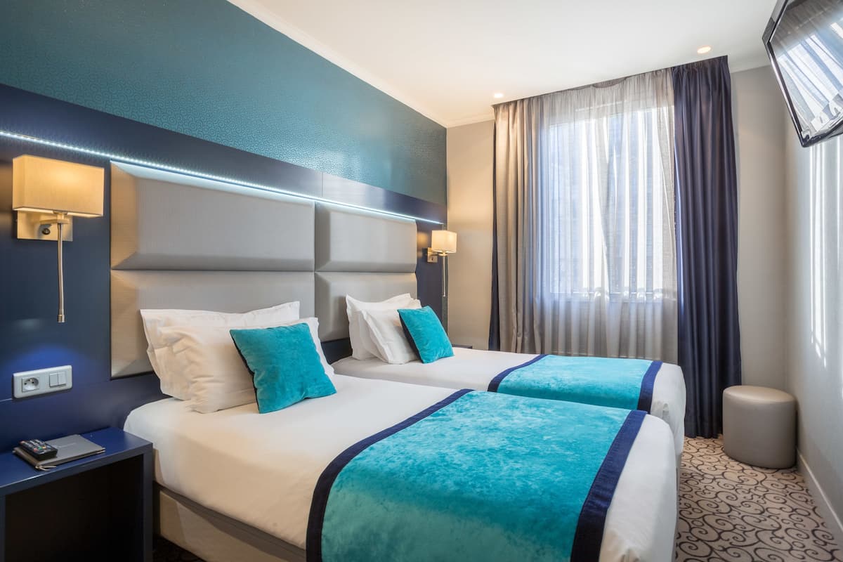 A hotel room with two beds, a nightstand, a lamp, a TV, and a large window with curtains.