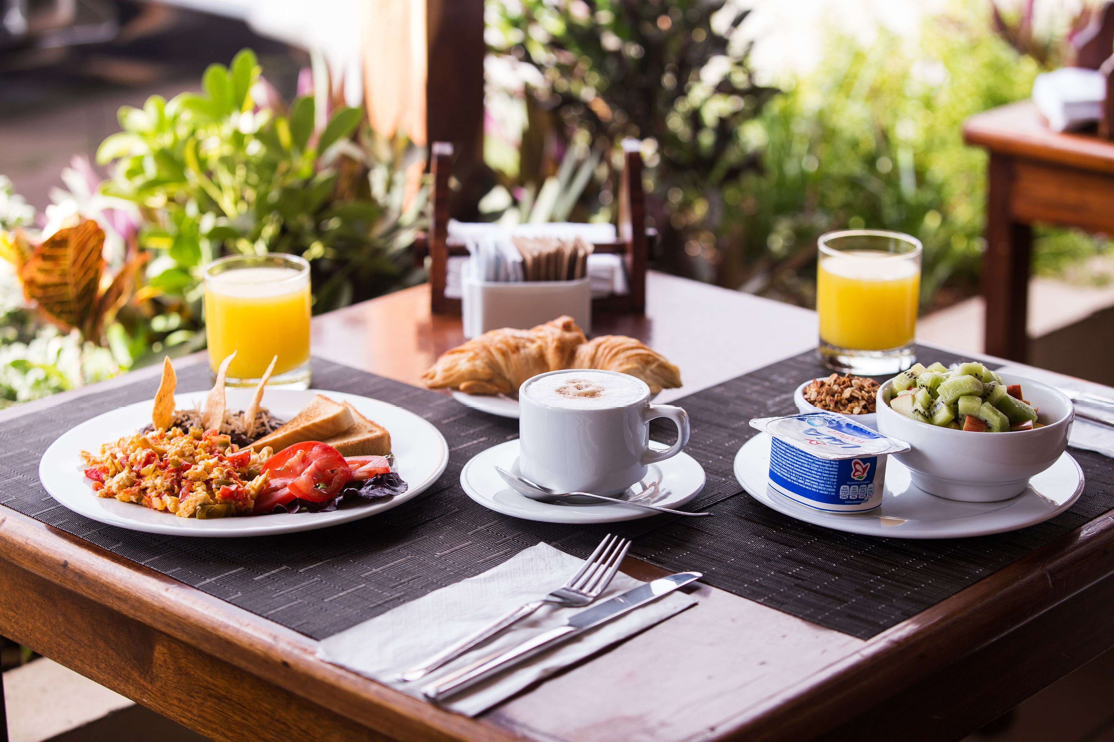 A breakfast table with plates of food, a cup of coffee, and a glass of orange juice.