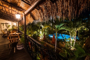 A wooden deck with chairs and tables, surrounded by lush tropical plants and a thatched roof structure. - La Pasion Hotel Boutique by Bunik (Playa del Carmen)