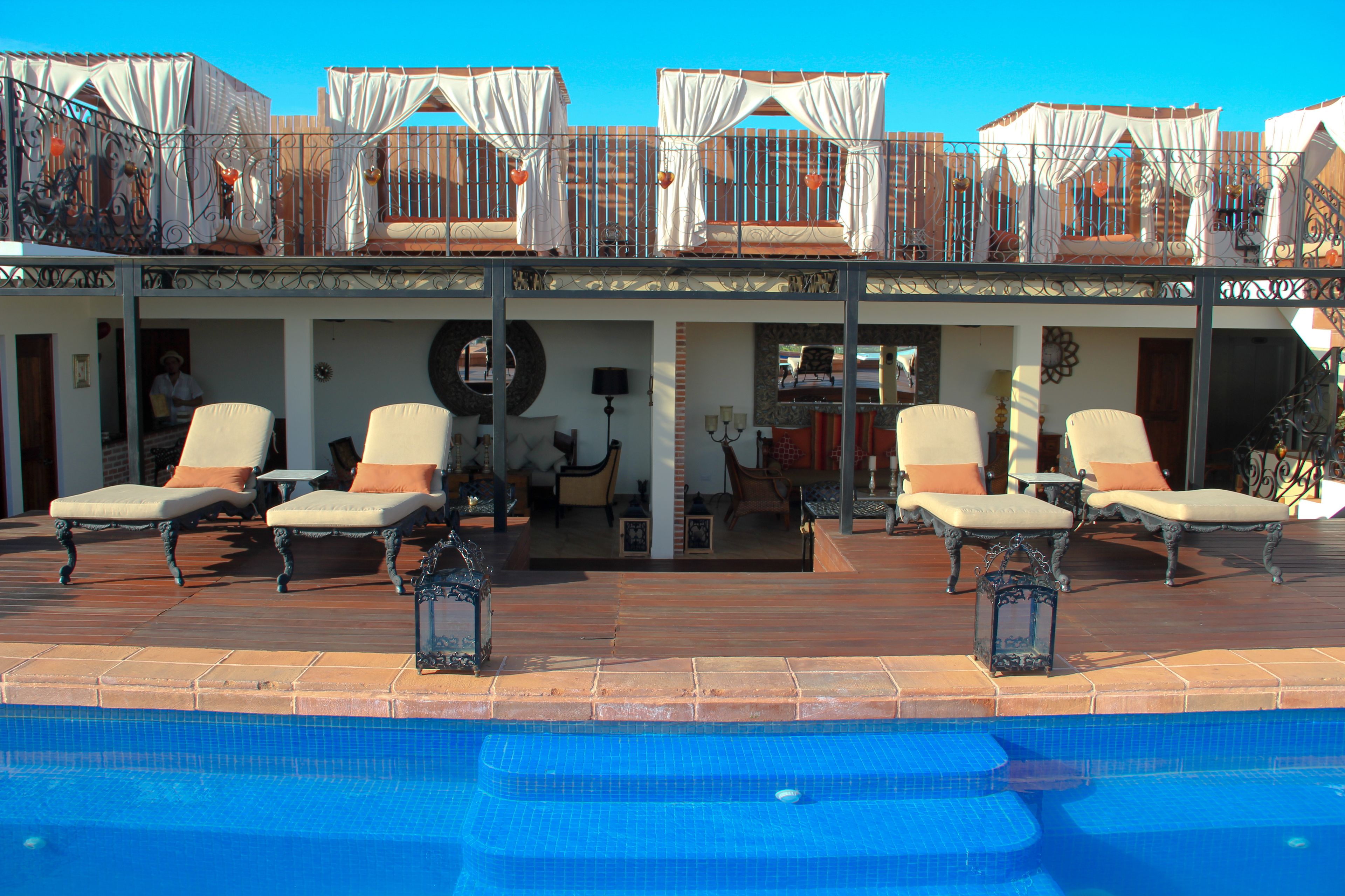 Un área junto a la piscina con sillones de descanso y una zona de estar cubierta al aire libre.