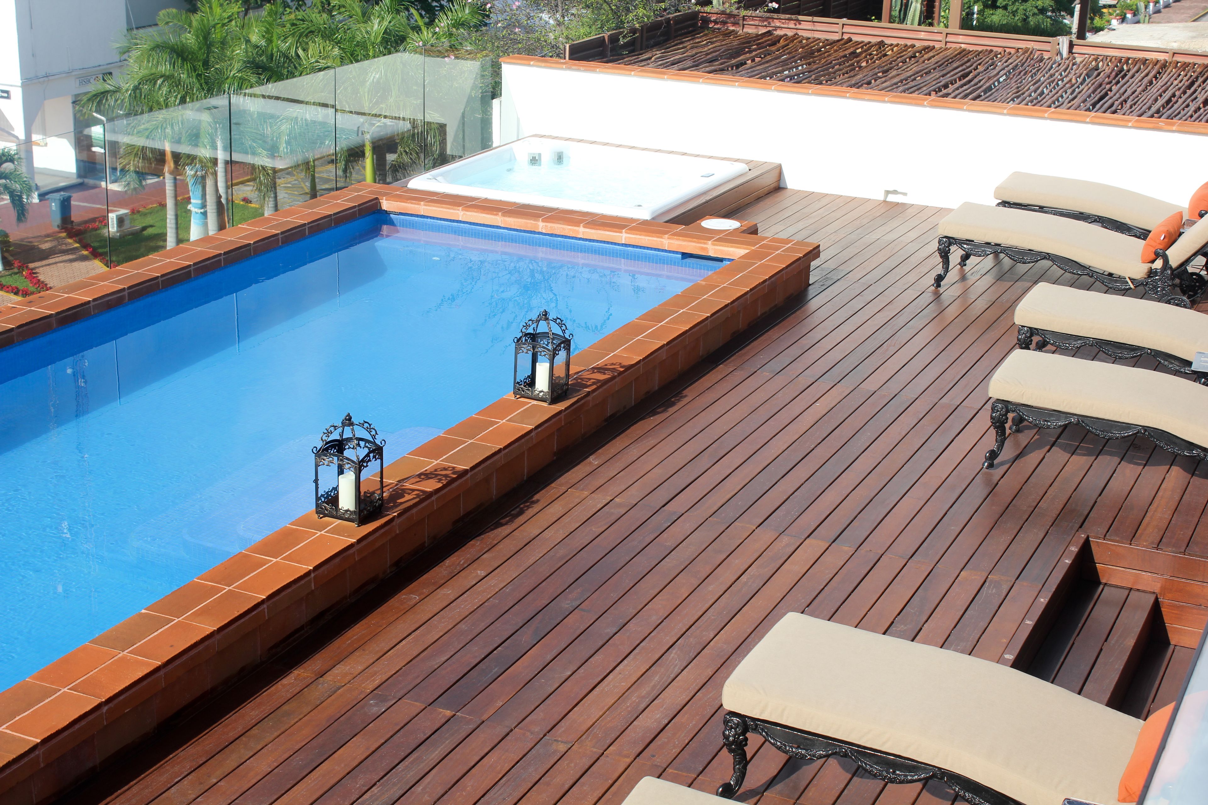 Une piscine sur le toit, avec une terrasse en bois, des chaises longues et un jacuzzi.