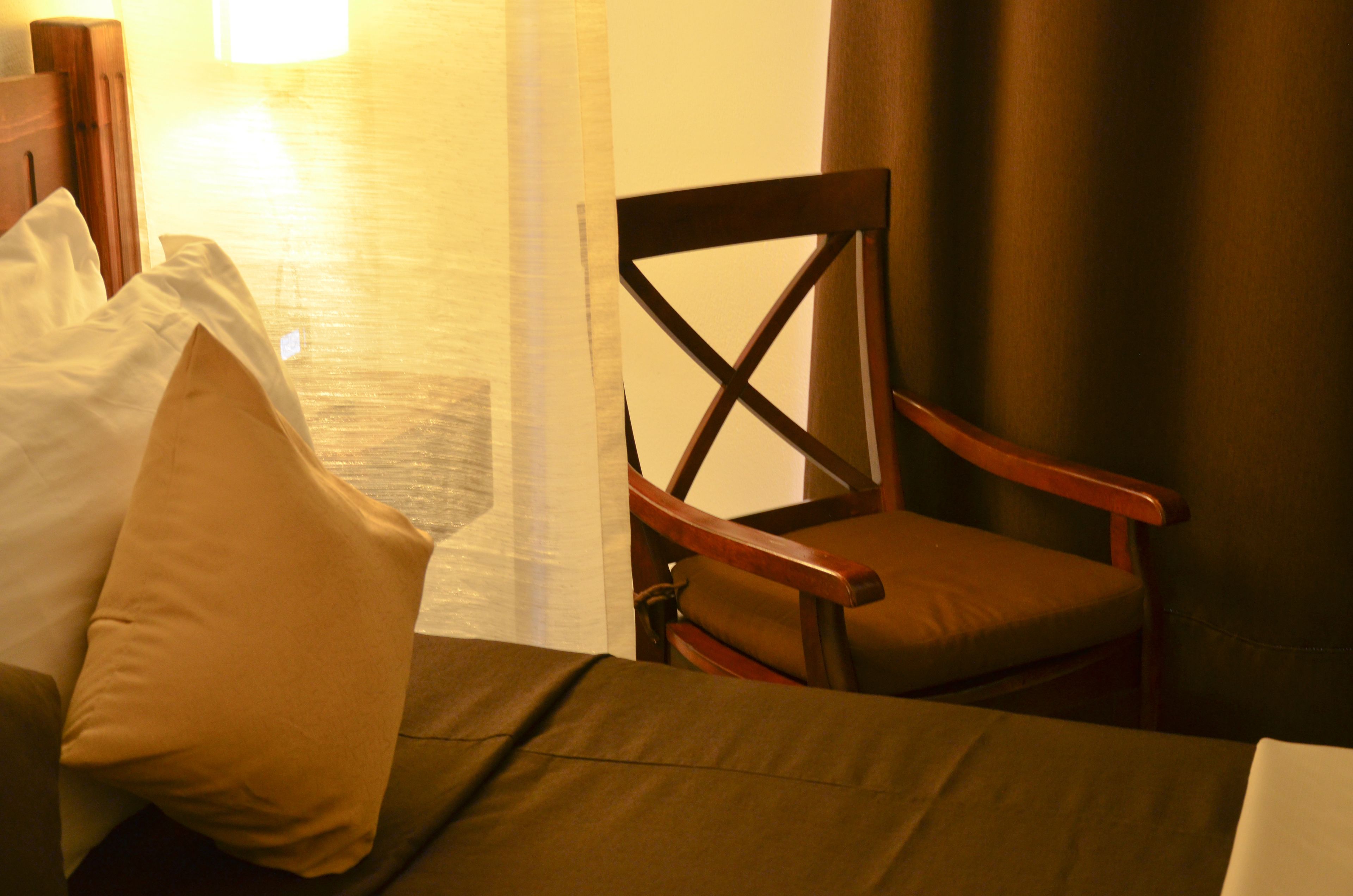 A hotel room with a bed, a wooden chair, and a curtain.