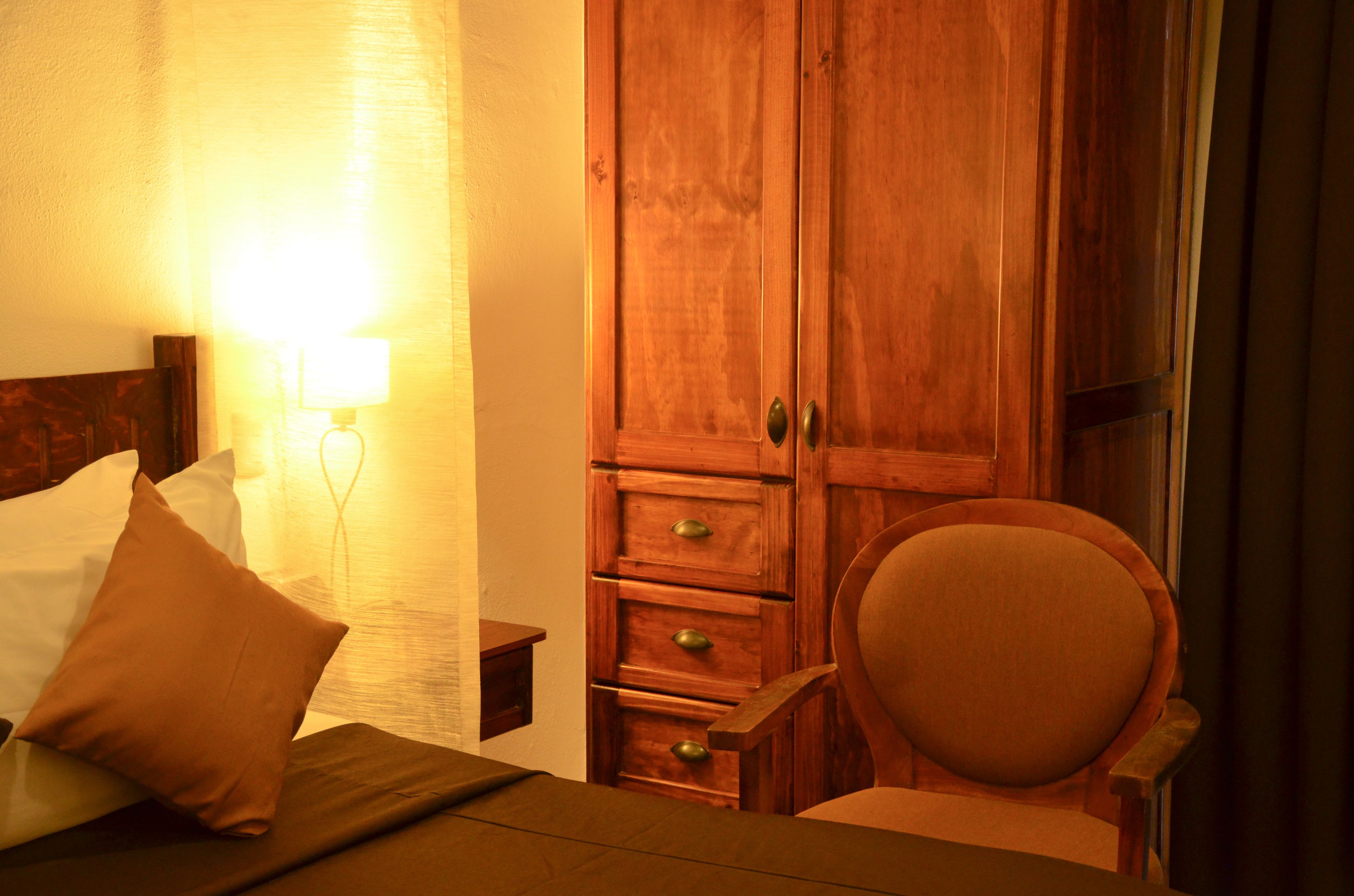 A hotel room with a bed, a nightstand, a wooden wardrobe, and a chair.