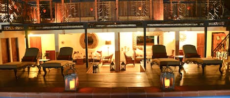 Zona junto a la piscina con sillas de descanso, una terraza de madera y una barandilla con detalles de metal decorativo.