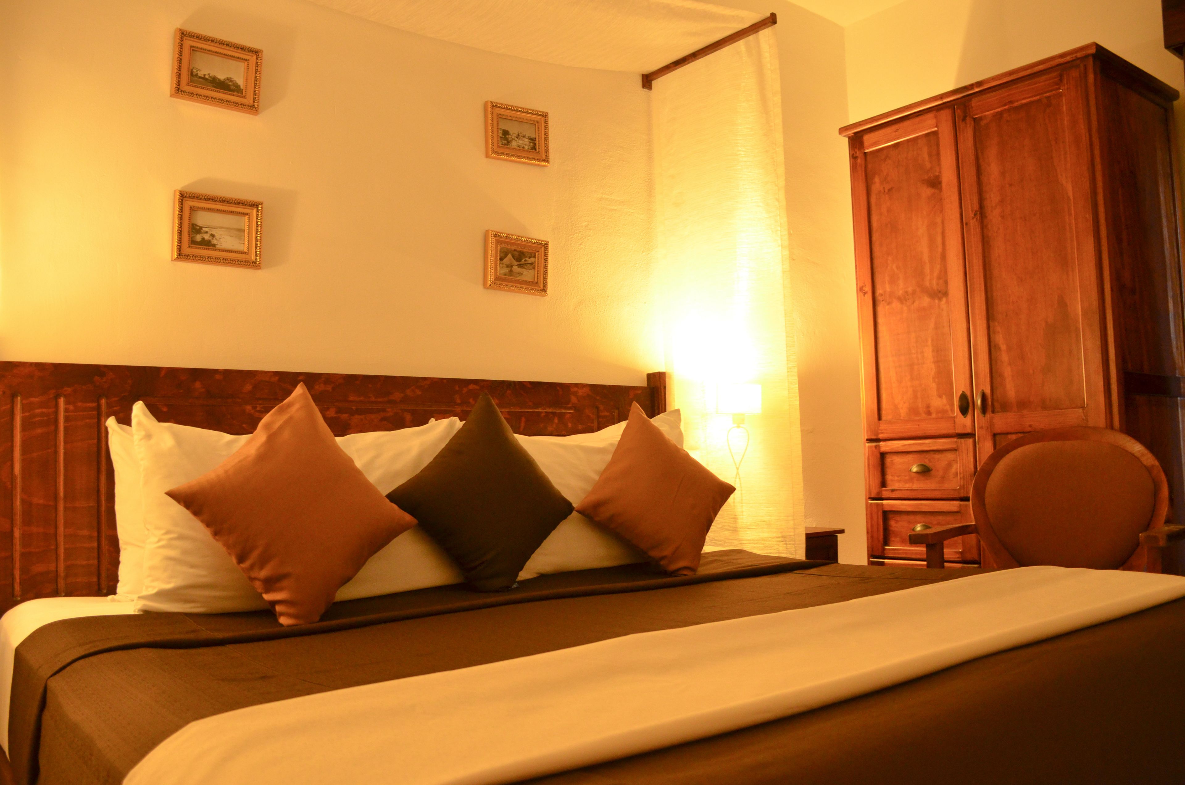 A neatly made bed with a wooden headboard, a wooden wardrobe, and framed pictures on the wall.