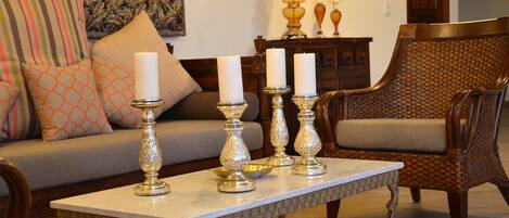 A living room with a sofa, patterned cushions, a coffee table with candles, and a wicker chair.