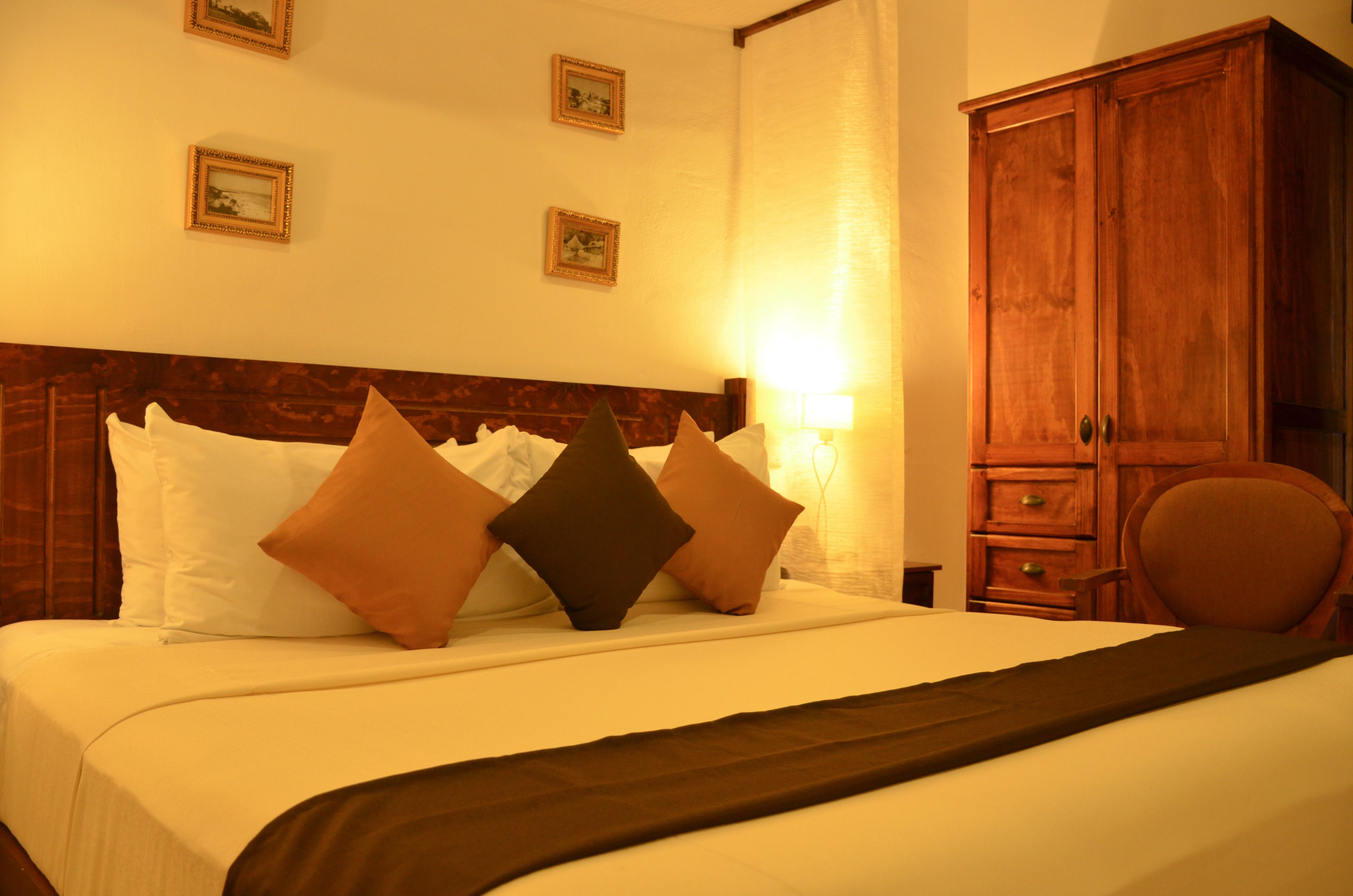 A hotel room with a large bed, a wooden headboard, a wardrobe, and a chair.
