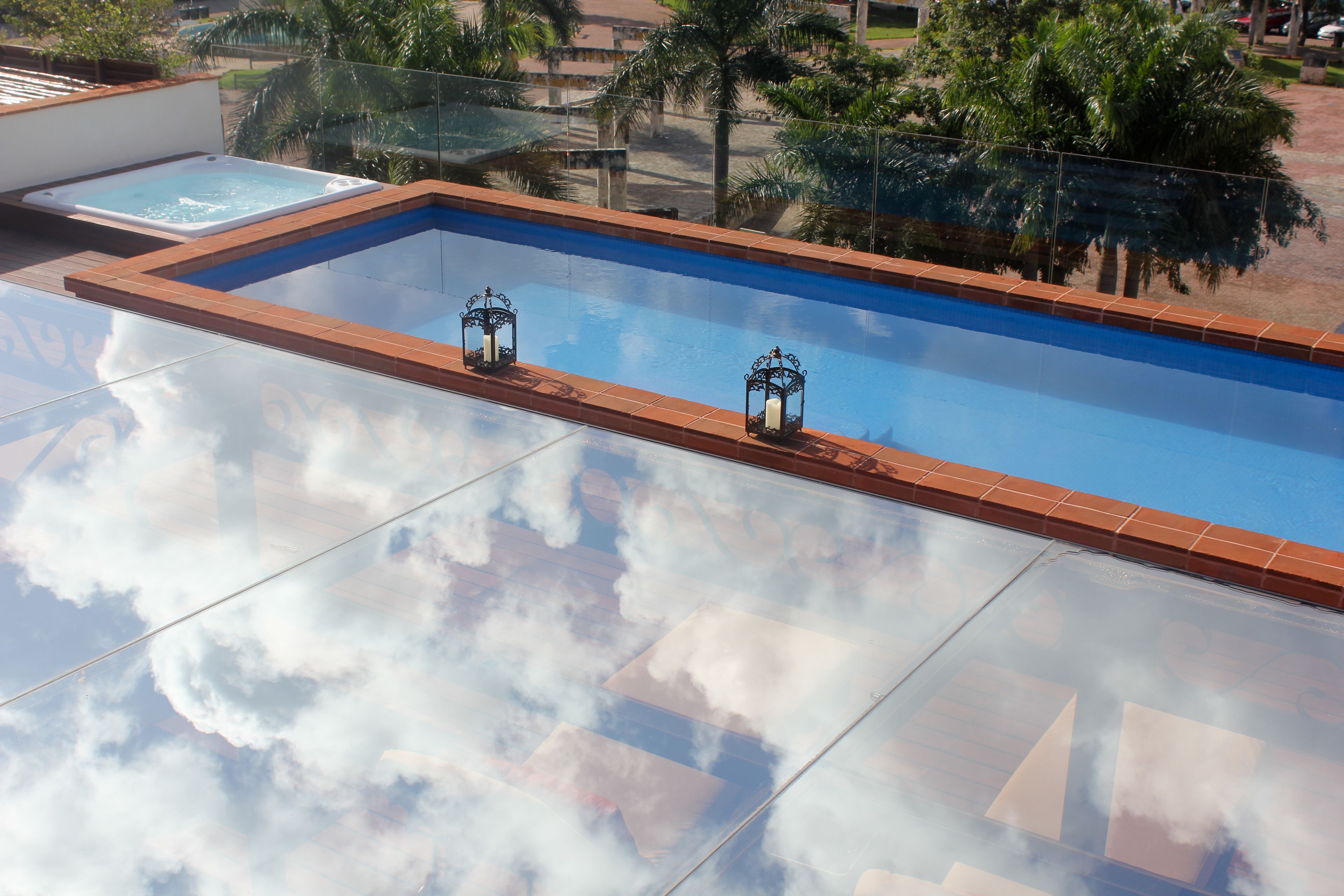 A rectangular pool with a tiled edge, two decorative lanterns, and a clear reflection of clouds on the pool's surface.