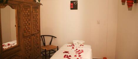 Una habitación con una cama, un armario de madera, una silla y una lámpara fijada a la pared.
