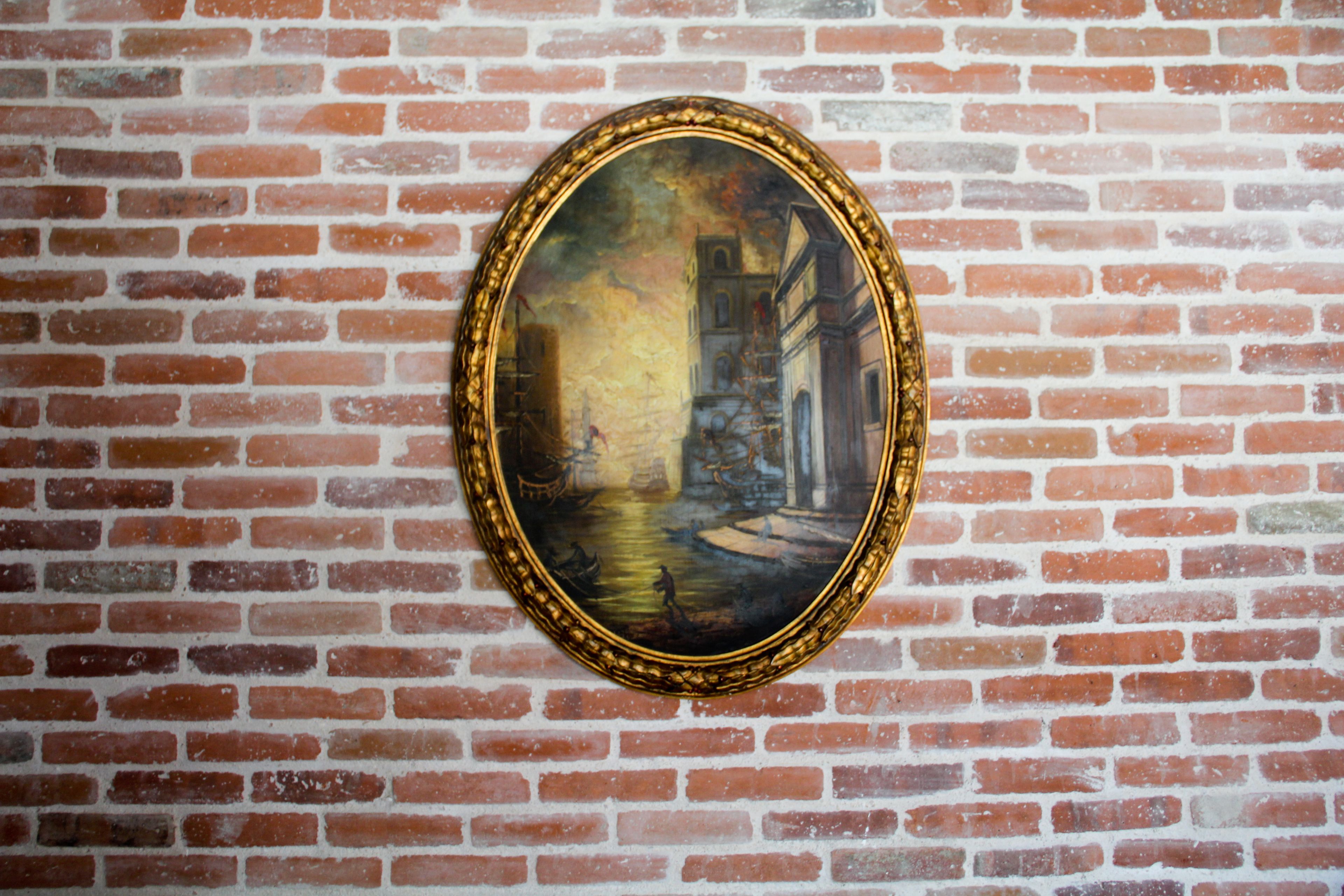 Un tableau encadré représentant une scène de canal, accroché à un mur de briques.