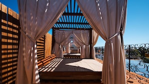 Una cama con cortinas blancas, suelo de madera y vistas a una piscina y jardín.