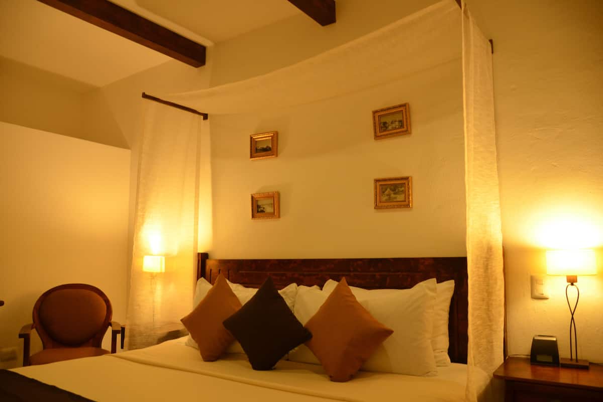 A hotel room with a bed, a chair, and a nightstand with a lamp.
