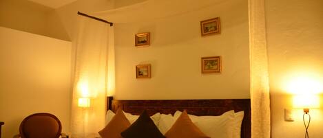 Quarto de hotel com uma cama, uma cadeira e uma mesa de cabeceira com abajur.