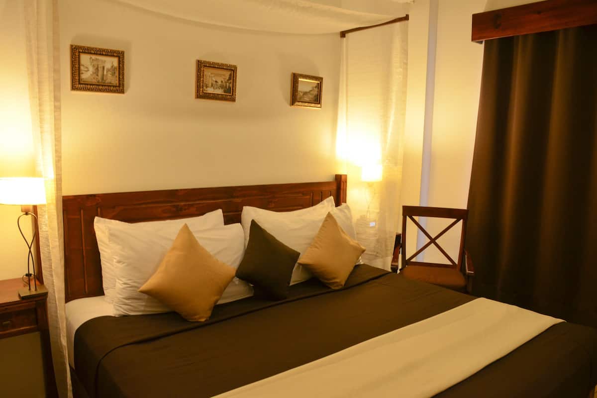 A neatly made bed with a wooden headboard, white and brown pillows, and a dark bedspread. There are framed pictures on the wall above the bed.