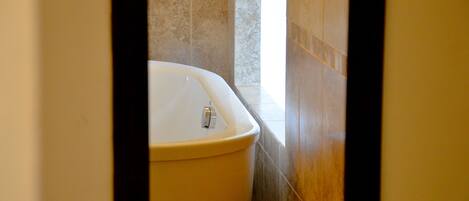 A bathroom with a white bathtub, tiled walls, and a wooden floor.