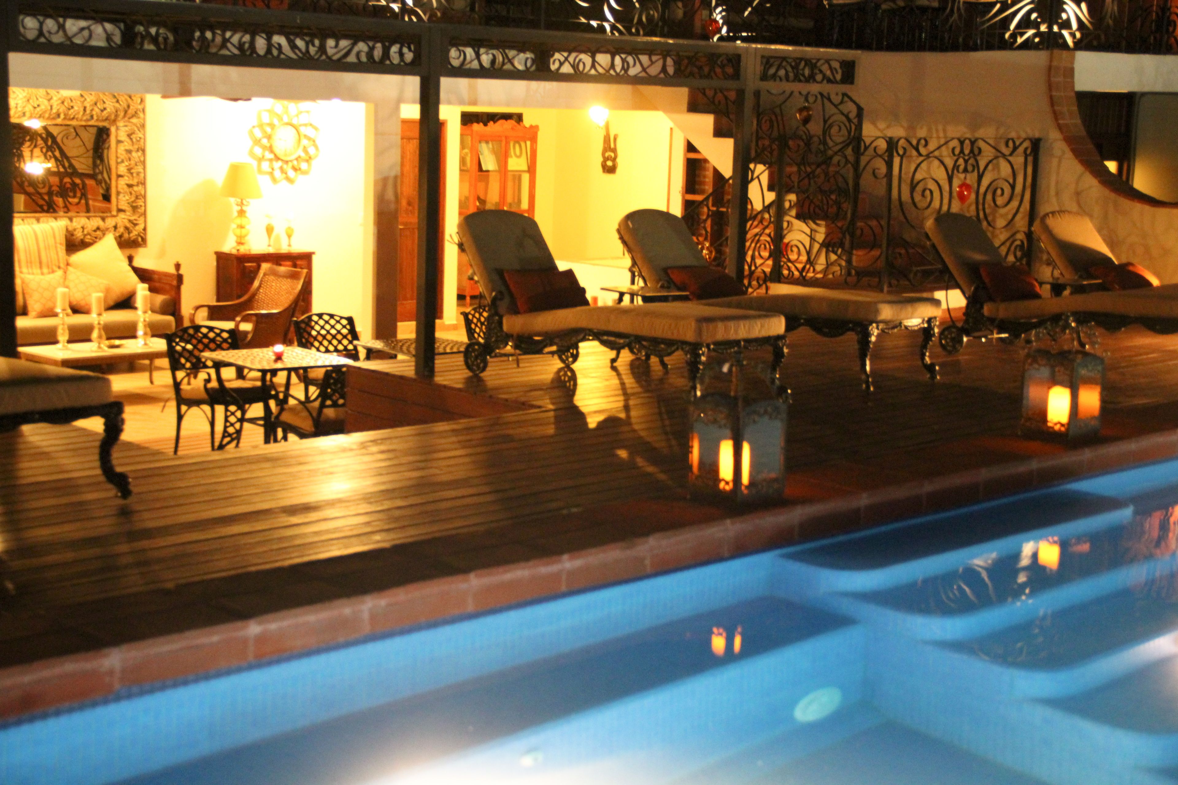 A poolside area with lounge chairs and a table, surrounded by a wooden deck and decorative railings.