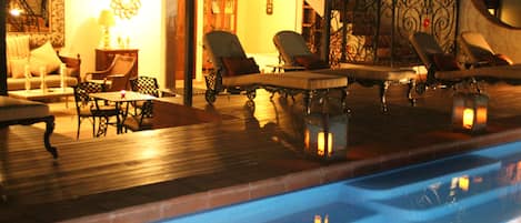 Un espace aménagé au bord de la piscine, avec des chaises longues et une table, entouré d’une terrasse en bois et de rampes décoratives.