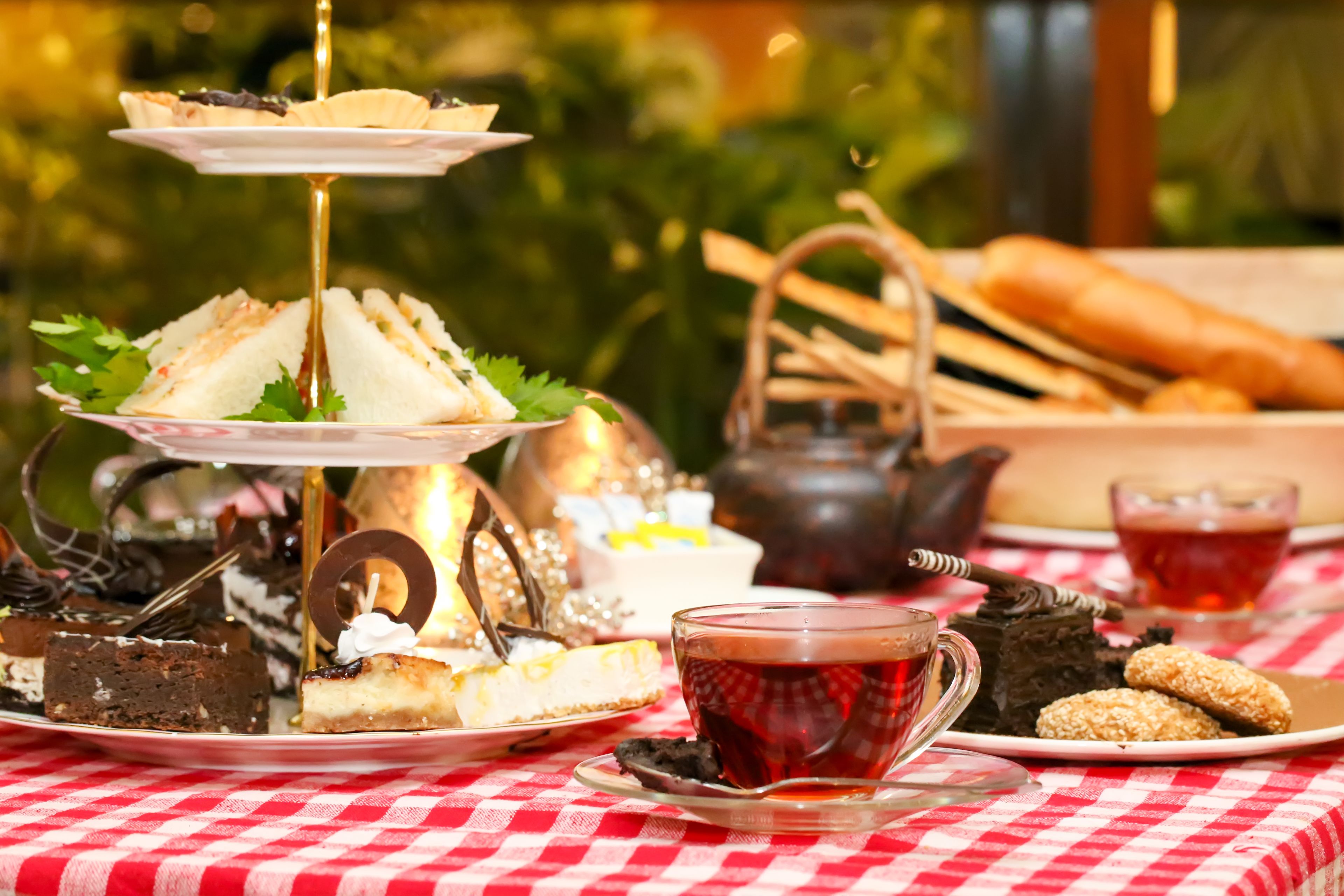 A tiered dessert stand with various pastries and a teapot on a checkered tablecloth.