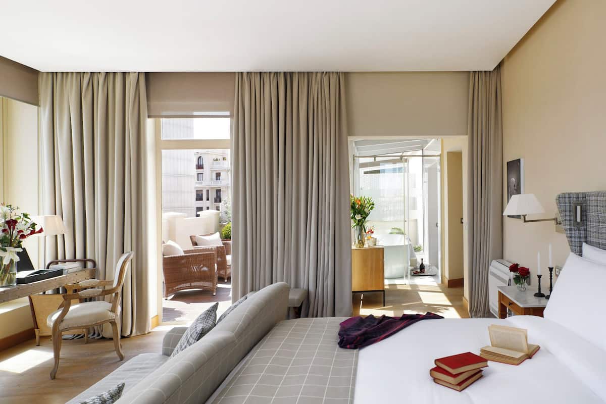 Quarto de hotel com cama, escrivaninha, cadeira e vista para a varanda externa.