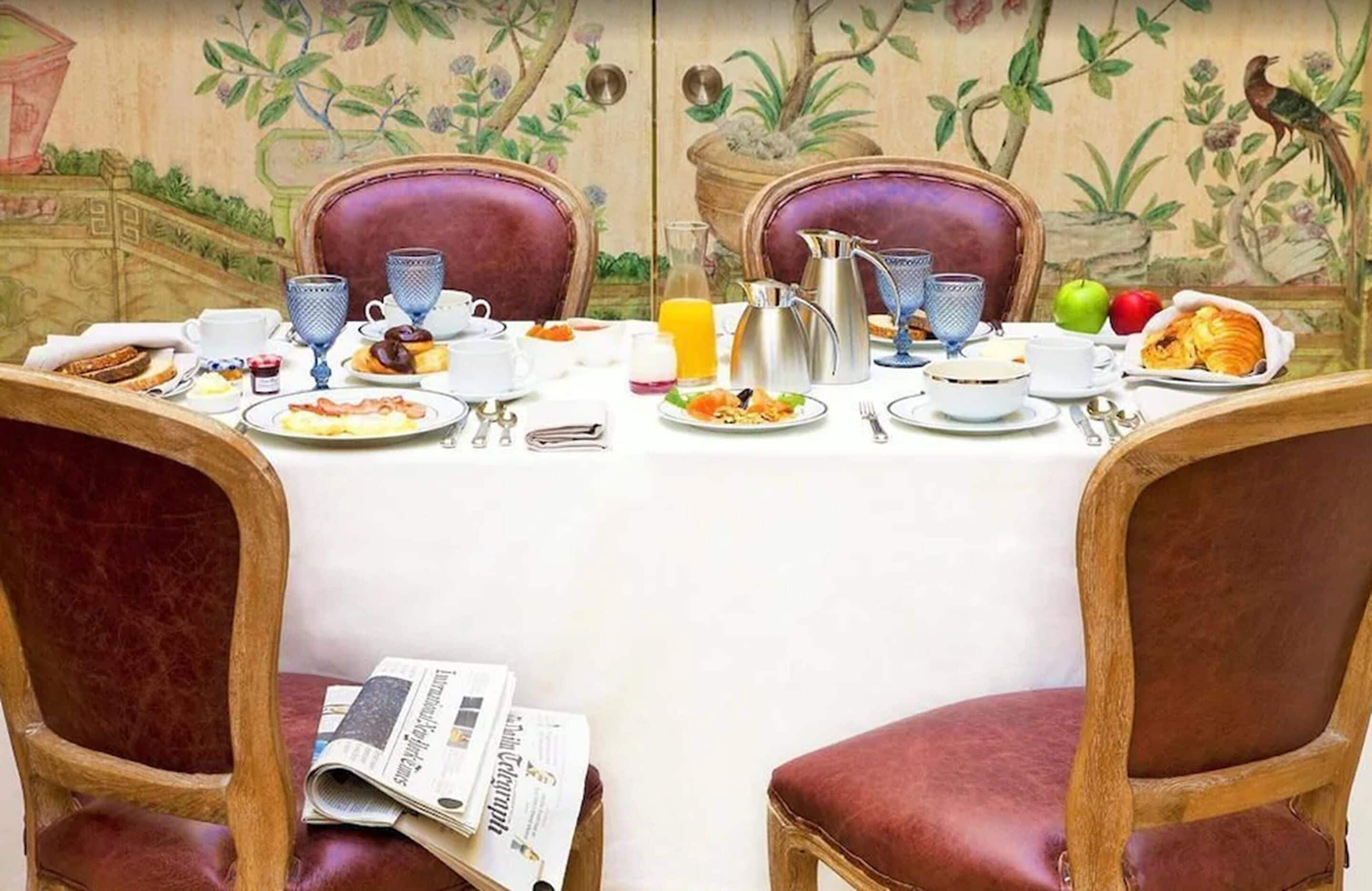 A breakfast table set with various dishes, cups, and a newspaper.