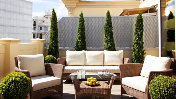 Una terraza en la azotea con mobiliario de mimbre, una mesa de centro de cristal y plantas en macetas.
