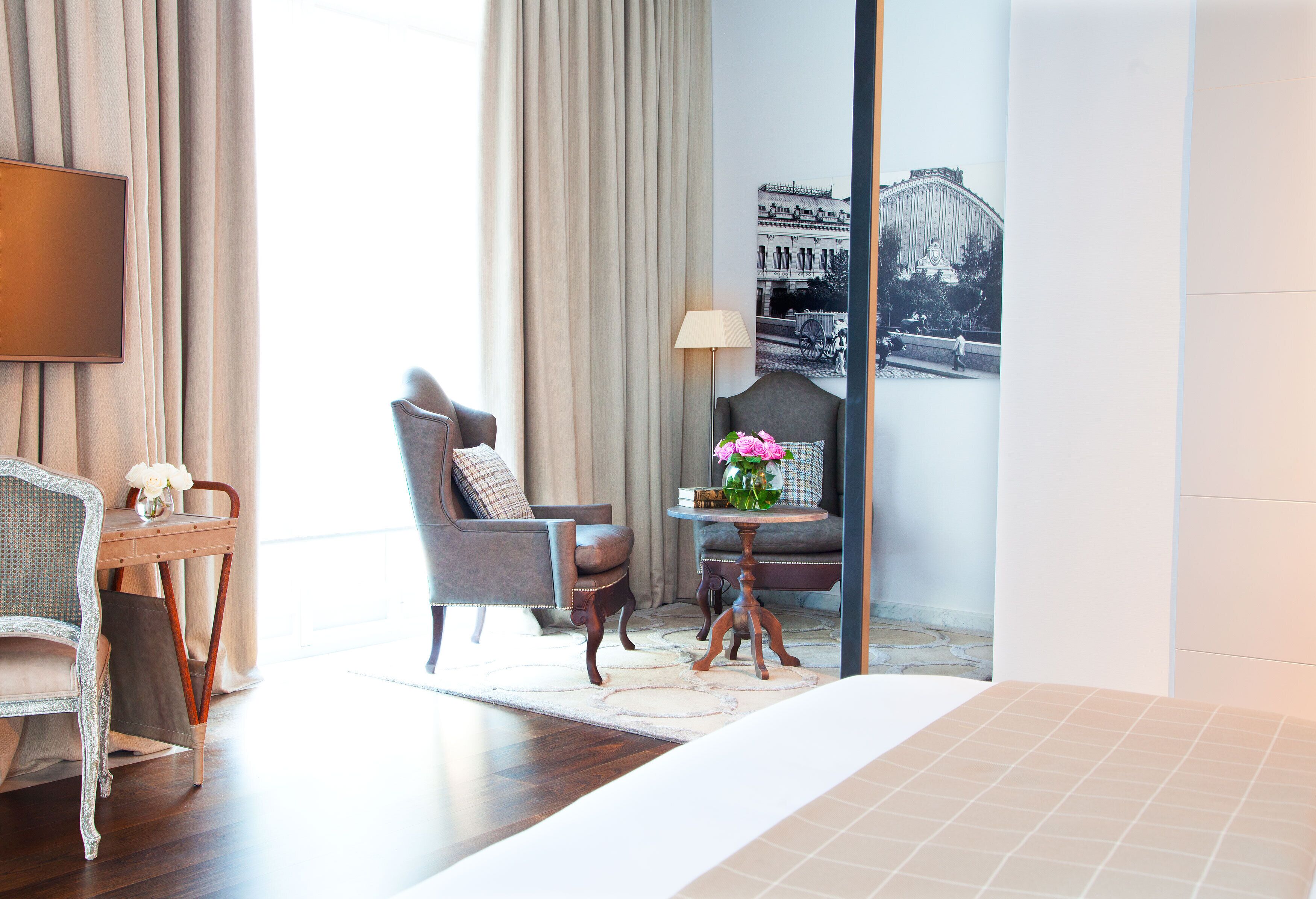 A hotel room with a large bed, a TV mounted on the wall, a seating area with a chair and a small table with a vase of flowers.