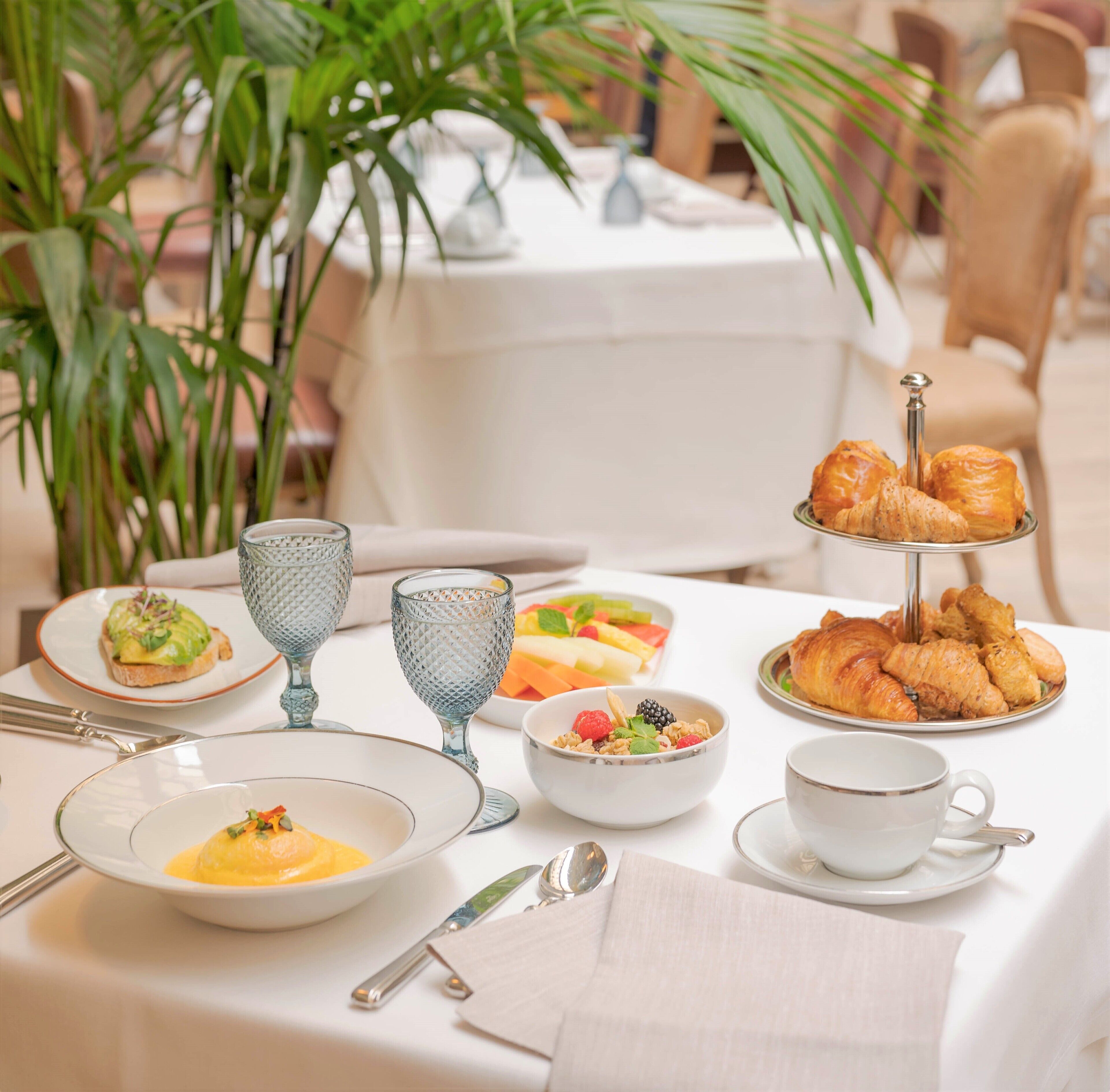 A dining table set with various dishes, including croissants, a bowl of fruit, and a glass of water.