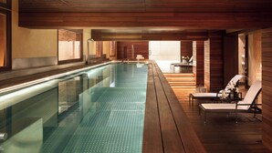 Una piscina interior moderna con paneles de madera, sillones de descanso y vistas al exterior.