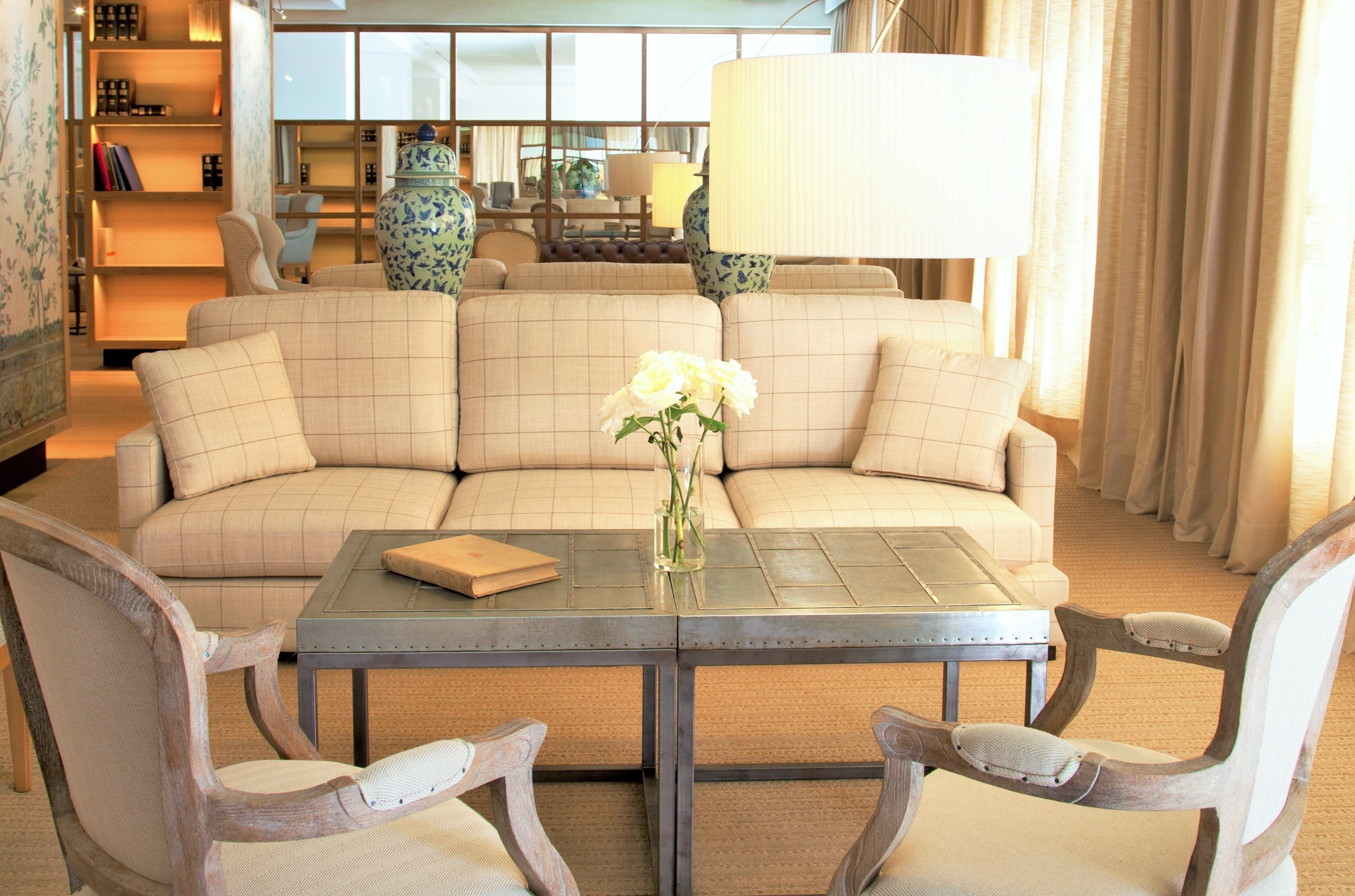 A living room with a beige sectional sofa, a glass-top coffee table, and two wooden chairs.