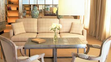 A living room with a beige sectional sofa, a glass-top coffee table, and two wooden chairs.