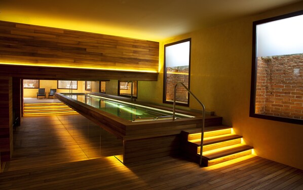A modern interior with a long, narrow pool, wooden flooring, and a staircase with illuminated steps.