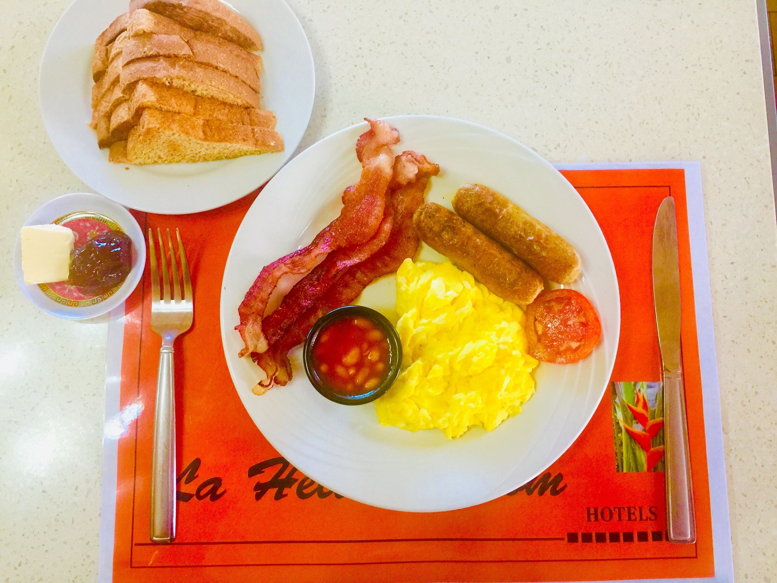 A breakfast plate with bacon, sausages, scrambled eggs, and toast.