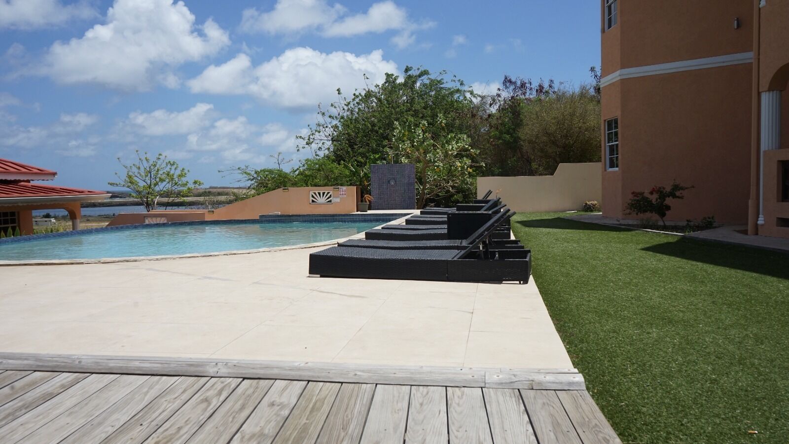 Un área de piscina con sillones de descanso, una terraza de madera y un edificio con tejado de tejas.