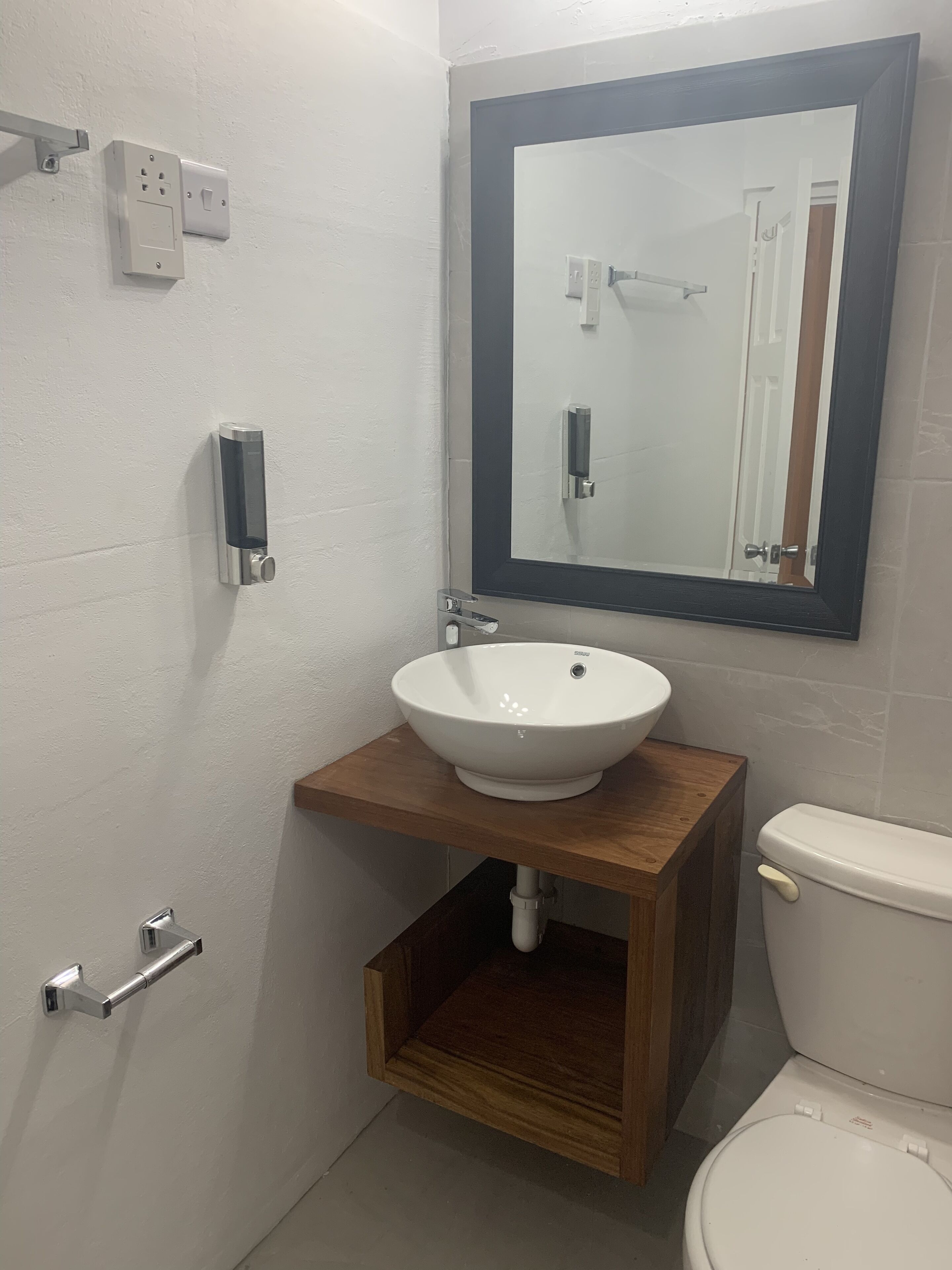 A bathroom with a white sink, a wooden vanity, a toilet, a mirror, and a wall-mounted light switch.