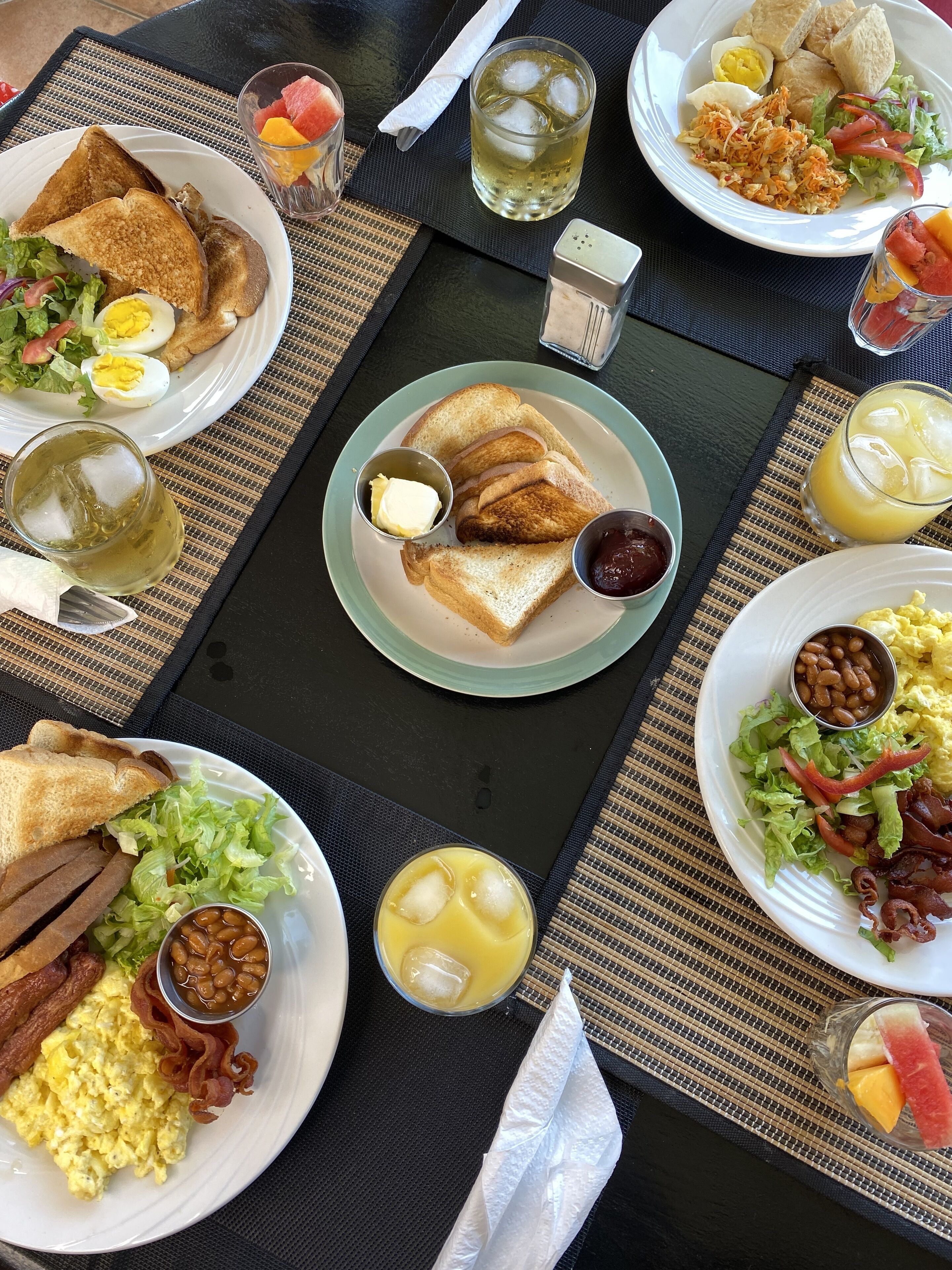 Une table dressée pour le petit-déjeuner, avec des assiettes contenant des toasts, des œufs, du bacon, des haricots et de la salade.