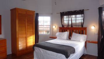 Un dormitorio con cama, armario de madera, ventilador de techo, ventana con cortinas e iluminación en la pared.