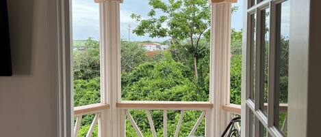A covered patio with two chairs and a table, a view of greenery and buildings, and a white door frame.