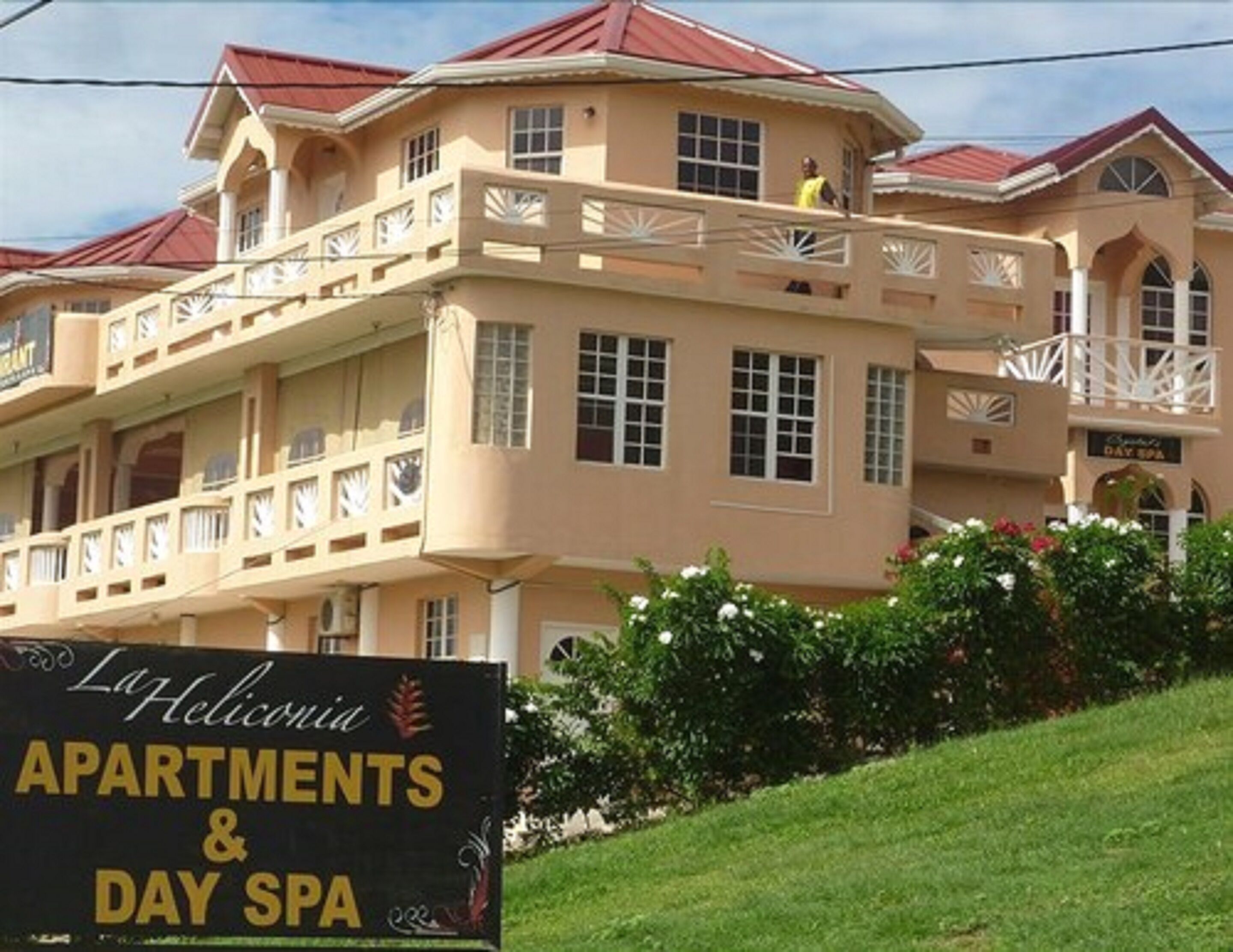 Un edificio de varios pisos con balcones, un letrero que indica Apartamentos y Spa La Heliconia, y un techo rojo.
