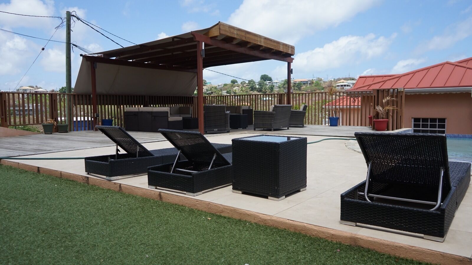 An outdoor patio area with black wicker furniture, a covered seating area, and a view of the neighborhood.