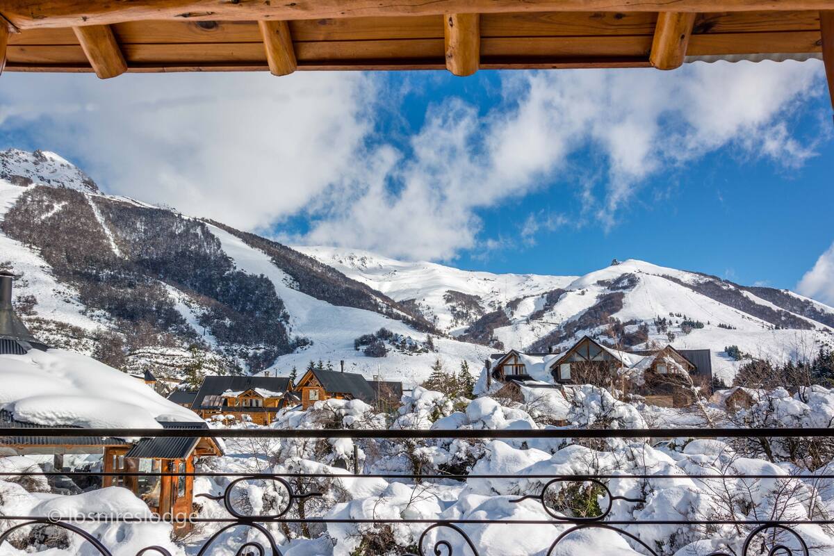 Paisaje nevado de montañas con cabañas de madera y una pérgola de madera.