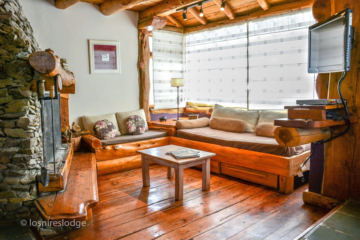 Una sala de estar acogedora con pared de piedra, muebles de madera y un televisor montado en la pared.